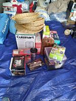 Photo showing variety of kitchenware items arranged on a tarp including baskets, boxed appliances, cutting boards, salad bowl and other kitchen accessories.