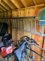 Aluminum extension ladder stored horizontally on wall studs in a wooden shed, alongside other tools and equipment