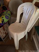 Stacked white plastic outdoor patio chairs with a slotted back design, showing dirt and need for cleaning.