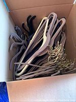 Box of multiple velvet clothes hangers in gray and black with gold hooks.