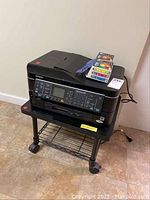 Full view of Epson WorkForce 635 printer on black wheeled stand with color ink cartridges on top