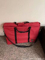 Red fabric carrying case with black handles and shoulder strap containing ferret cage.