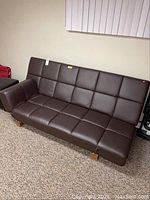Full view of brown adjustable futon with back and sides down, on carpeted floor underneath a window with blinds.