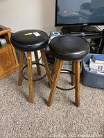 Two swivel top bar stools with black round cushioned seats and wooden legs, showing minor scratches.