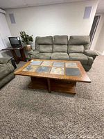 Rectangular wood coffee table with six stone insets in two rows of three on top. Surrounding furniture includes greenish reclining sofas on carpeted floor.