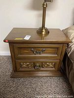 Front view of vintage wood nightstand showing two drawers and decorative metal handles. Worn finish visible.