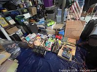 Overall view of assorted items on blue tarp showing electronics, boxed products, DVDs, and household items