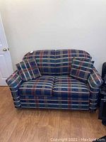 Front view of a plaid loveseat with two matching pillows on wooden floor against a light-colored wall.