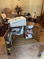 Wooden sewing cabinet with open double doors showing items inside, including box of threads.