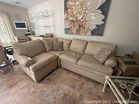 Front angle view showing left chaise and main seating area of beige Ethan Allen sectional sofa, placed in living room environment with tiled flooring and floral wall art.