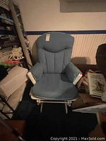 Front view of wood rocking chair with blue upholstered padded cushions on seat and backrest in dim setting.