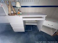 Front angle view showing desk three drawers and keyboard pull out. Desk placed on blue carpet with lamps and small decorations on top. Wall with striped wallpaper in background.