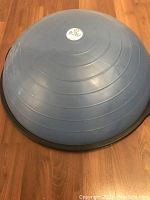 Angled view of the blue Bosu ball balance trainer showing the side profile including the black plastic base and blue inflatable dome.