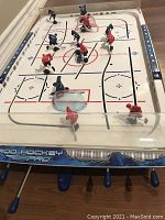Full view of the Franklin Rod Hockey Pro table hockey game on a hardwood floor. Shows plastic rink and players on rods with handles.