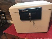 Closed beige Sentry home safe with black locking panel and key inserted in the lock.