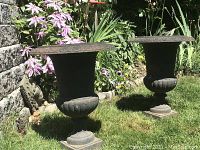 Pair of urns on grass in front of a stone wall with purple clematis blooms.