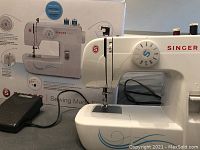 Singer Start 1304 sewing machine shown with foot pedal and original box packaging in background. Clean and intact with visible stitch selection dial.
