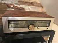 Front view showing woodgrain top and brushed aluminum front panel with tuning dial and signal meters