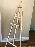 Full standing wooden easel showing overall structure and height against a wall.