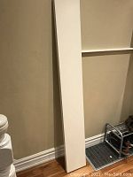 Full length vertical view of the white IKEA Lack shelf leaning against the wall near a shoe rack, showing its slim profile and clean edges.