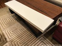 Top view of rectangular white floating shelf on carpeted floor in front of furniture showing the smooth white surface and size.