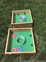 Opened view showing wooden game box with green surface, central ring, and red and blue discs inside