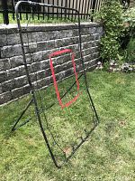 Full black metal frame baseball trainer with red rectangular target net, showing adjustable angle and netting setup.