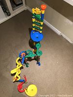 Overview of large tall marble run toy assembled on carpet floor, featuring interconnected colorful plastic pieces and funnels.