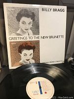 Front cover of the vinyl album showing art portraits and the title 'Greetings to the New Brunette' by Billy Bragg.