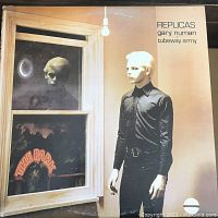 Front cover of the vinyl album 'Replicas' featuring a man in black standing by a window with reflections and signage saying 'The Park'