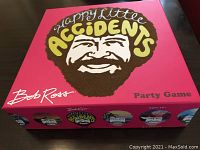 Top view of the closed game box showing Bob Ross illustration and game title on bright pink background.