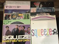 Top-down view of 11 vinyl records from the 1980s, alternative and pop genres. Visible album covers include The Boomtown Rats, Thomas Dolby, Squeeze, 10cc, Split Enz, and The Lilac Time.