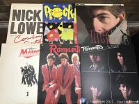 Front view of six vinyl record covers stacked, showing titles by Nick Lowe, The Romantics, The Motors, Rockpile