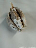 View of three fish sculpture from above, showing heads and tails forming a circle with textured scales and carved details.