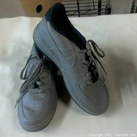 Left and right chocolate brown Nike Air Force 1 shoes positioned one leaning on the other showing upper and main side profile.