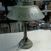 Full view of the vintage olive green metal toleware table lamp showing the painted acorn and leaf motif on the wide shade, base, and stem. Lamp is shown upright with cord coiled at base.