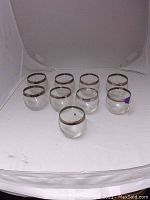 Nine mid-century roly poly glasses with sterling rims arranged in a group, clear glass, showing some tarnish on the rims.