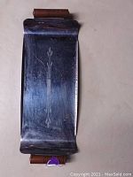 Full view of rectangular metal cigarette rolling tray with curved edges and wooden handles at both ends. Surface has etched vertical decorative motif. Shows scratches and wear.
