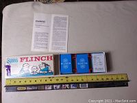 Image of the box open showing two decks of Flinch cards in blue holders and an instruction pamphlet alongside a measuring tape.