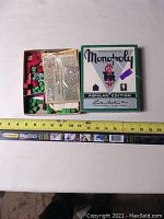 Original Monopoly Popular Edition box with contents inside including wooden game houses and hotels, cards, and money shown with ruler for scale.