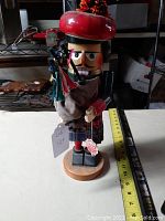 Front view of the nutcracker showing red tam hat, facial details, red clothing, tartan kilt, and bagpipe held in hands.