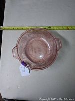 Top-down view of pink depression glass bowl showing floral pattern and two handles, with measuring tape for size reference.