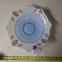 Top-down view of vintage clear depression glass dish showing baby blue inlay center with embossed floral patterns, scalloped edge with milky white glass and hand-painted pink flowers around rim.