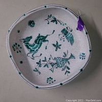 Top view of the salt glazed dish showing teal and green hand painted designs including a doe, vase, hand, and floral elements.