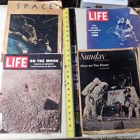 Four vintage magazines about America's space exploration arranged closely with a measuring tape showing scale, highlighting LIFE On The Moon, and Sunday Herald Traveler 'Men on the Moon'