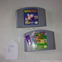 Photo of two Nintendo 64 game cartridges, Super Mario 64 and Yoshi's Story, both with visible label art and some signs of use.