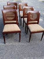 Set of six wooden dining chairs with cane oval backs arranged on pavement.