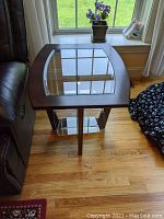 Side table showing wood frame and glass top, positioned beside couch and window.