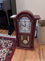 Front view of Waltham wooden case clock on wooden floor, showing arched top and glass door.