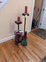 View of three hurricane glass candleholders holding red candles and a tall narrow neck vase on wooden floor against wall